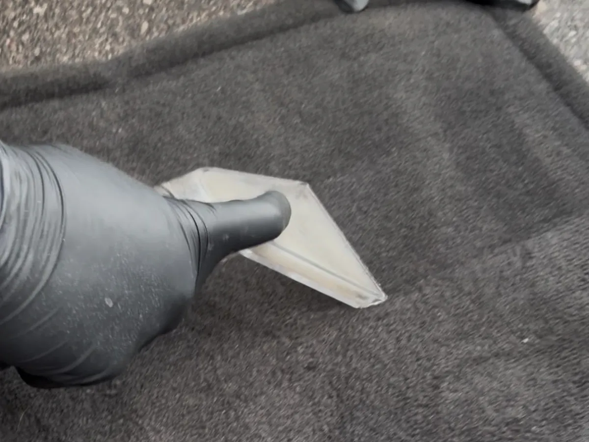 Gloved hand working a hot water extraction tool across a car floor mat during a deep clean