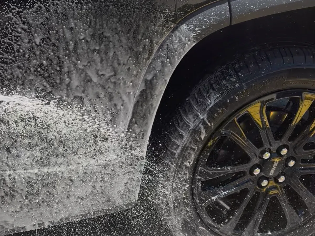 Foam covering the lower door and alloy wheel of a dark SUV partway through a hand wash